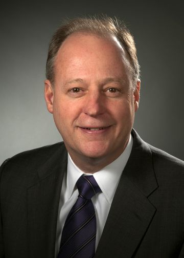 John McGovern head shot, wearing a black suit and purple tie